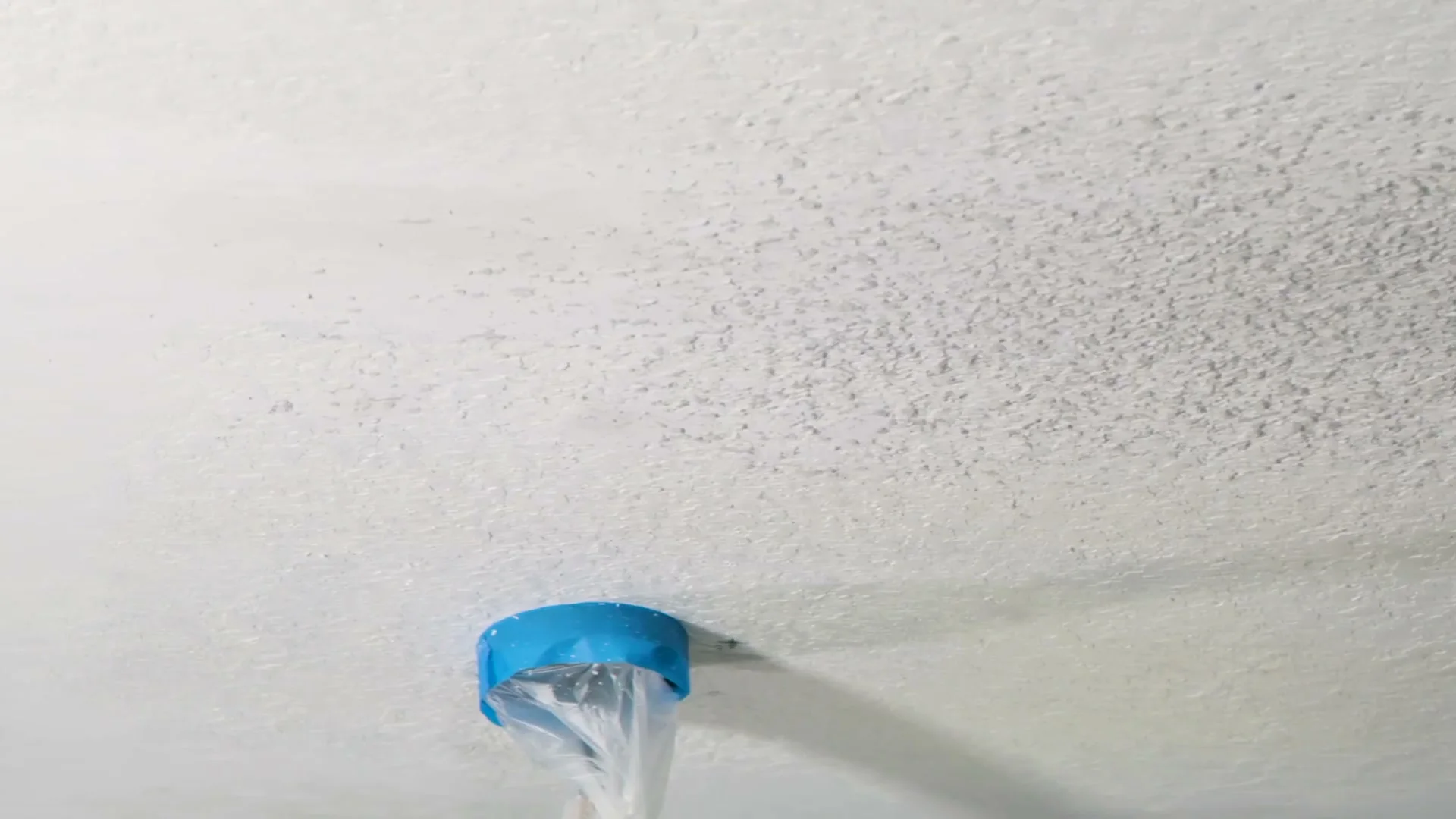 A finished popcorn-style ceiling around a taped-off fixture box.